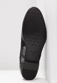 Semelle de chaussure habillée noire avec des grips texturés, nom de la marque "ANNA FIELD" et taille 37 embossés près du talon.