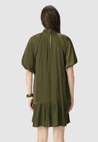 Vestido corto verde oliva con mangas abullonadas, espalda con abertura en forma de lágrima y dobladillo con volantes en capas. Fabricado en una tela suave y ligera.