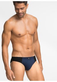 Slip blu navy con fascia nera, caratterizzato da righe verticali e un'etichetta con il logo. Realizzato in tessuto morbido, progettato per il comfort.