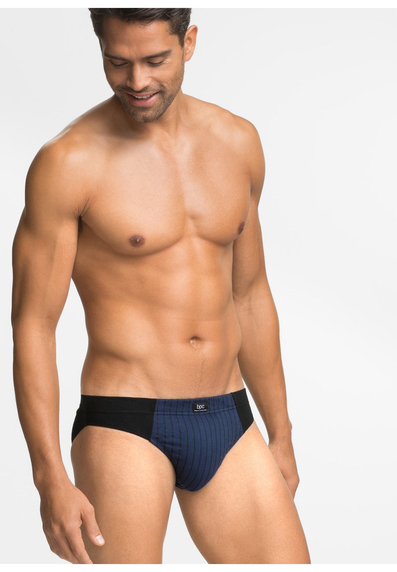 Slip blu navy con fascia nera, caratterizzato da righe verticali e un'etichetta con il logo. Realizzato in tessuto morbido, progettato per il comfort.