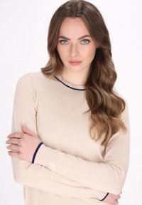 Beige pitkähihaisessa neuleessa on pyöreä kaula-aukko, ja siinä on kontrastina ja tekstuurina tummansinistä koristekangasta kauluksessa ja hihoissa.