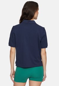 Marineblauwe polo met korte mouwen, klassieke kraag en een zijsplit aan de zoom, gemaakt van een zachte, gestructureerde stof.