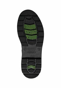 La suela de goma de la zapatilla presenta un patrón de relieve profundo, predominantemente negra con detalles en verde, texturizada para ofrecer agarre, con la etiqueta "remonte" y tamaño 37.