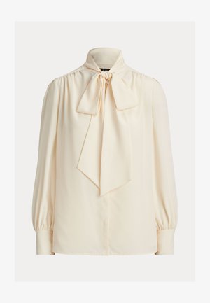 Μπλούζα μακριά μανίκια σε κρεμ χρώμα με ψηλό λαιμό και μεγάλο δεμένο φιόγκο στο γιακά, με ραμμένους φουσκωτούς ώμους και μανσέτες με κουμπιά.