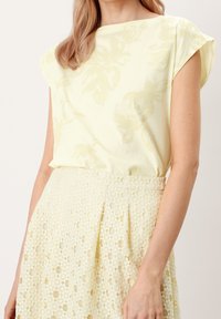 Světle žlutý top s květinovým vzorem a krátkými rukávy v kombinaci s texturovanou sukní ve stylu krajky ve shodné barvě, která má sklady.