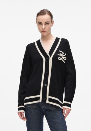 Cardigan nero a maglia con bordo bianco, collo a V e cinque bottoni. Presenta un logo sul lato sinistro del petto e una texture a coste.