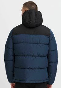 Marineblå pufferjakke med sort skuldersektion og hætte. Kviltet design, elastiske manchetter og nederste kant for isolering og komfort.