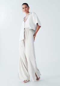 Lekka, off-white, oversize koszula zapinana na guziki z kołnierzykiem, w połączeniu z luźnymi, zwiewnymi spodniami z elastycznym pasem i rozcięciami.