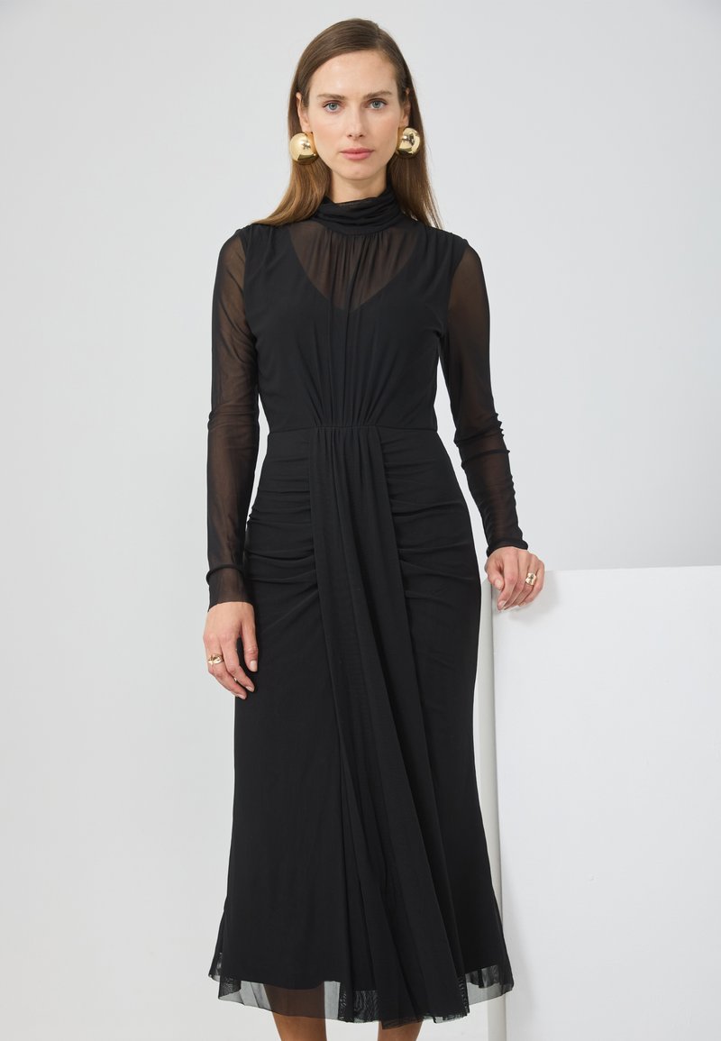 Μαύρο φόρεμα με μακριές διαφαν�είς μανίκες και ψηλό λαιμό. Διαθέτει σχεδιασμό με draped σχήμα και συγκεντρωμένο ύφασμα, καθώς και διαφανή ύφανση στο κάτω μέρος. Χρυσά εντυπωσιακά σκουλαρίκια.