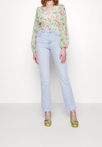 Blumenmuster-Wickeloberteil in Grün und Rosa, hochgeschnittene hellblaue Jeans und grüne Plateauschuhe. Mit Puffärmeln und V-Ausschnitt.