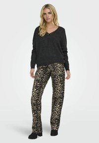 Tamno siva, teksturirana pletena majica s V-izrezom, u kombinaciji s hlačama s leopard uzorkom u boji bež i crnoj. Model nosi crne platforme.