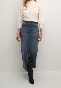 Jupe longue en denim avec une fente devant, dotée d'une ceinture et d'un lavage bleu délavé. Accompagnée d'un pull en maille crème avec un motif texturé.