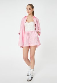 Lyserød stribet skjorte, hvid blondecamisole og matchende lyserøde shorts; shorts med snor, og modellen bærer hvide sokker og sneakers.