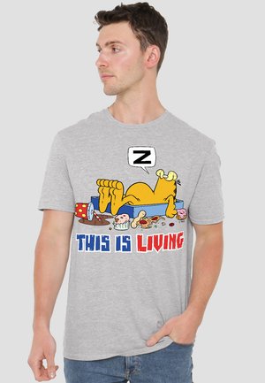 Gray short-sleeve t-shirt featuring a cartoon cat lounging with food items. Text reads "THIS IS LIVING" in red and blue bold letters.