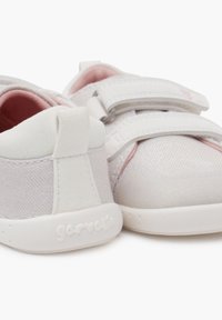 Zapatillas de lona blancas con acentos en rosa, que cuentan con correas de velcro, un acabado texturizado y una suela de goma. Logo en relieve en el talón.