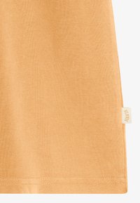 T-shirt orange à manches courtes en tissu doux, avec une coupe épurée et une petite étiquette de marque cousue sur le bas à gauche.