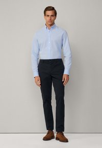 Lichtblauwe overhemd met knopen, donkere slim-fit broek en bruine suède schoenen. Eenvoudig ontwerp, klassieke snit en soepele texturen.