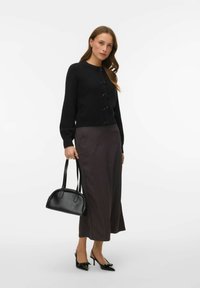 Melnas adītas kardigans ar loku pogām, kopā ar tumšu svītrainu svārku. Tur mazu melnu somu, valkā melnas smailas augstpapēžu kurpes.