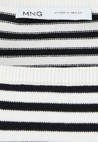 Tissu tricot rayé noir et blanc avec une étiquette de vêtement indiquant MNG, taille EU-USA S, MEX CH.