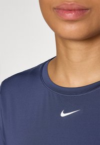 Tamno plavi atletičarski majica s okruglim izrezom i ravnim šavovima, istaknuta bijelim Nike logom na prsima. Glatka tekstura.