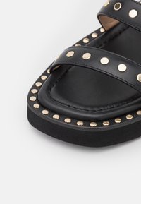 Sandale plateforme en cuir noir avec des clous dorés le long des brides et du bord, dotée d'un bout carré et d'une semelle intérieure rembourrée.