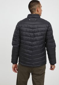 Veste doudoune noire pour homme avec un design matelassé, col montant, boutons-pression et texture lisse. Les coutures visibles ajoutent un détail.