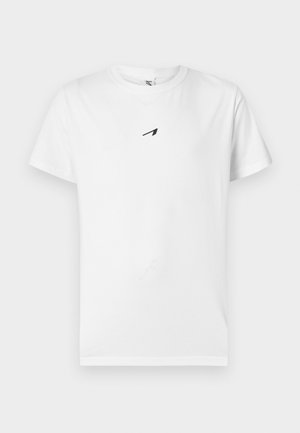 Dreadlocks-s férfi hátulról áll, fehér pólót visel fekete grafikával és szöveggel: "INNOVATION INCLUDED", valamint szürke nadrágot.