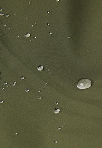 Tessuto verde oliva resistente all'acqua con gocce d'acqua sulla superficie, che mette in evidenza una texture liscia e una finitura opaca.