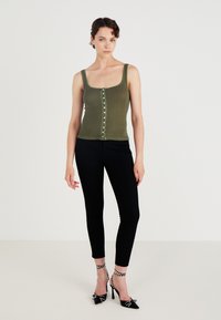Olive green ribbed tank top with square neckline, front button closure, and textured trim, paired with black fitted pants and polka dot heels.