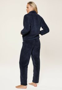 Navy-blaues, flauschiges Loungewear-Set mit einem Chevron-Muster. Die Jacke hat einen hohen Kragen und die Hose hat einen lockeren Schnitt, beide aus weichem Material.