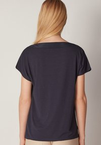 Mörk marinblå topp med kort ärm, tillverkad av mjukt material och med en avslappnad passform. Har en bred halsringning och en subtil lyster längs kragen.