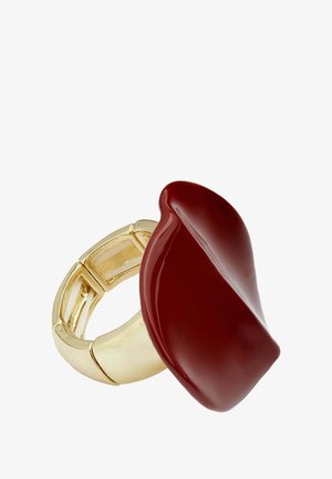 Dikke ring met een grote rode, glanzende lipvormige bovenkant en een gladde goudkleurige band. Het ontwerp heeft een unieke, moderne esthetiek.