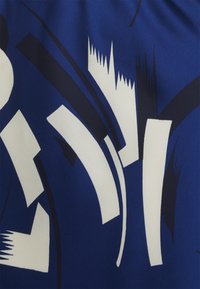 Modrá látka s abstraktními bílými a námořnickými vzory s zakřivenými a ostrými tvary, která zvýrazňuje různé textury a designy.