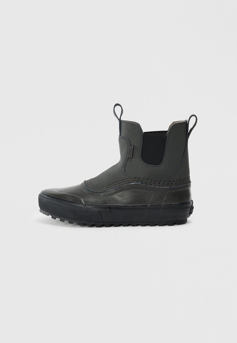 Bota media de goma y tela negra con tiradores, paneles laterales elásticos y suela de tracción resistente, mostrada en perfil lateral.