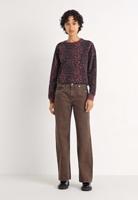 Leopárdmintás pulóver sötétlila és fekete színben; magas derekú, barna, bő szárú farmerrel párosítva; a modell egy semleges színű háttér előtt áll.