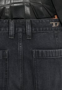 Jeans in denim scuro con una consistenza liscia e una finitura leggermente sbiadita, caratterizzati da due tasche anteriori e un accento con logo metallico sulla cintura.