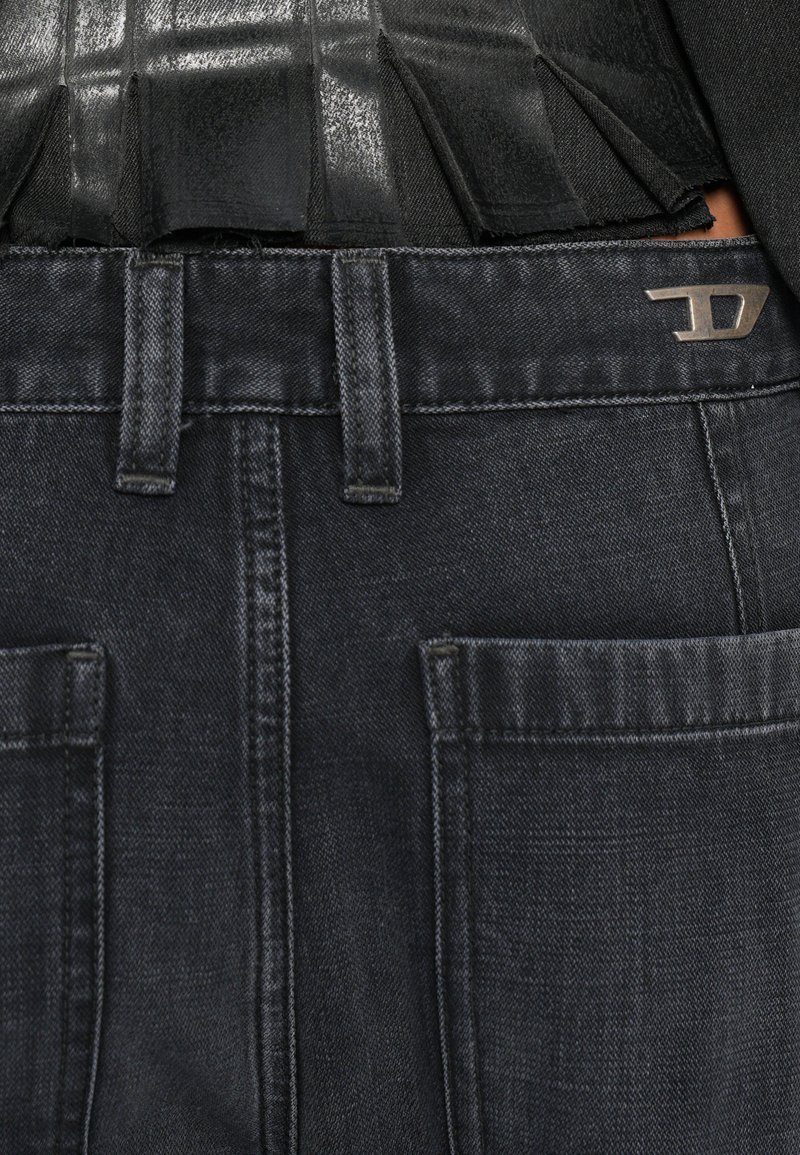 Dunkelblaue Jeans aus Denim mit glatter Textur und leicht verblasstem Finish, ausgestattet mit zwei Vorder taschen und einem metallischen Logo-Akzent am Bund.
