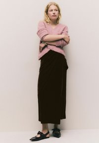 Rosa, flauschiger Pullover, langer brauner Samtenrock mit Drapierung und schwarze Slingback-Schuhe mit einer Schleifendetail. Minimales Design und weiche Texturen.