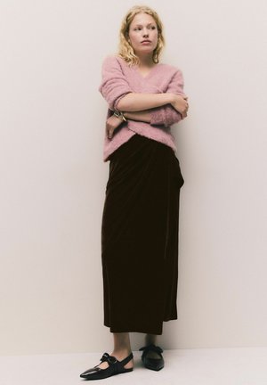 Rosa, flauschiger Pullover, langer brauner Samtenrock mit Drapierung und schwarze Slingback-Schuhe mit einer Schleifendetail. Minimales Design und weiche Texturen.