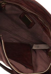 Interno di una borsa a mano in pelle borgogna, con una fodera in tessuto morbido, chiusura con zip e una piccola tasca per carte. Finiture della zip in colore oro.
