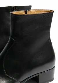 Las botas de cuero negro hasta el tobillo presentan una textura suave, punta redondeada y un tacón bajo y cuadrado. El interior es de un color marrón claro que contrasta, con una cremallera lateral.