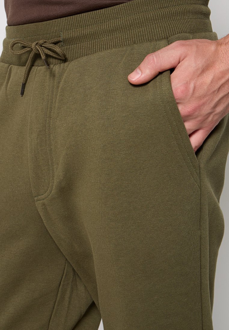 Pantalons de survêtement vert olive en tissu doux, avec une taille côtelée, un cordon de serrage et des poches latérales angulaires.