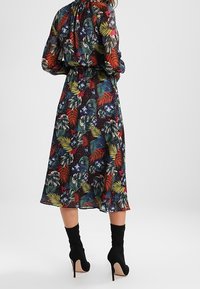 Robe maxi florale avec un fond sombre, ornée de motifs de feuilles colorées. Manches longues et taille cintrée, associée à des bottes noires à talons hauts.