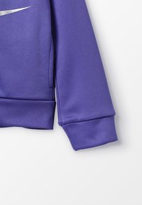 Lilla atletisk jakke med en struktureret overflade, der har et sølvlogo, ribbede manchetter og et afslappet pasformdesign.