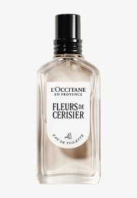 Transparent glaskanna med svart lock. Har en vit etikett med svart text. Innehåller en ljusfärgad vätska som representerar doften av körsbärsblommor.