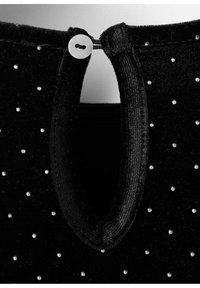 Svart sammetsplagg med en rund öppning bak, fäst med en knapp. Dekorerad med små silvernitar genom hela plagget.