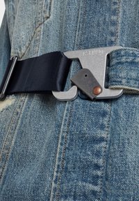 Tejido de denim con un acabado texturizado, que presenta una hebilla gris metálica y una correa de cinturón azul marino oscuro, asegurada por un acento de color cobre.