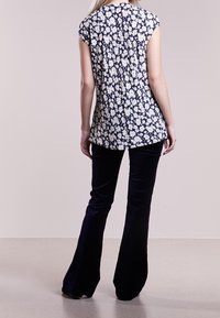 Marinblus med blommor och korta ärmar, kombinerad med utsvängda svarta byxor. Blusen har ett vitt blommönster och en längre bakre fåll.