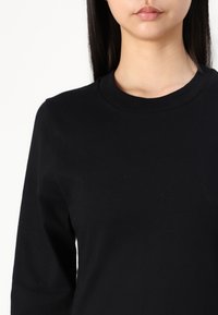 Svart langermet topp laget av myk stoff. Har rund hals og strukturert materiale med en glatt finish. Ingen synlige mønstre eller detaljer.