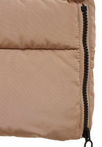 Sac matelassé beige avec texture capitonnée, comportant une fermeture éclair noire sur un côté et une finition mate. La couture est régulièrement espacée.